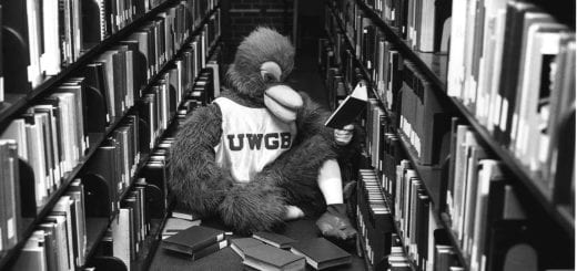 1980s black and white photo of Phlash the Phoenix Mascot reading books in the library stacks