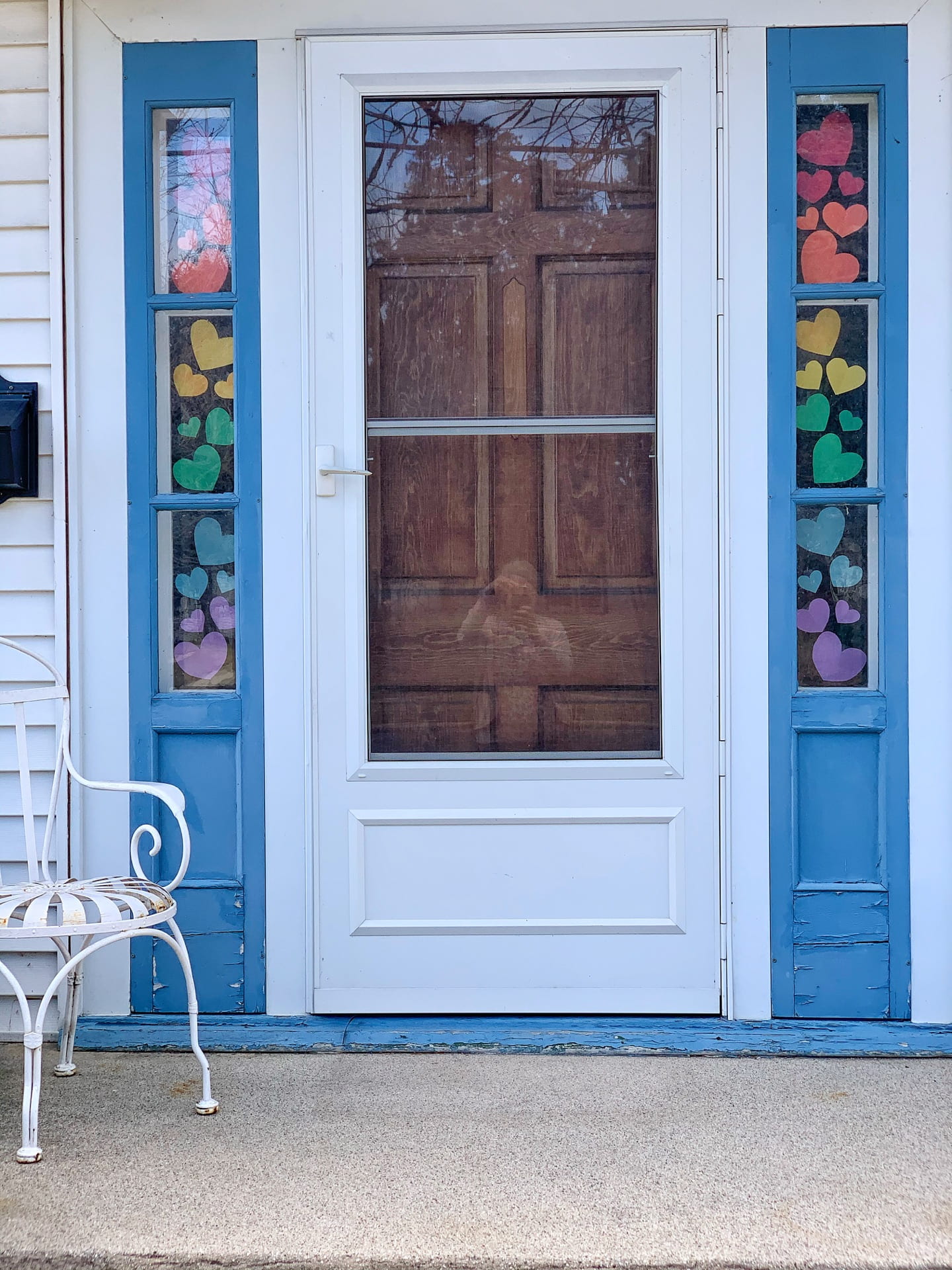 Front door with colorful paper hearts taped to the side-light windows.