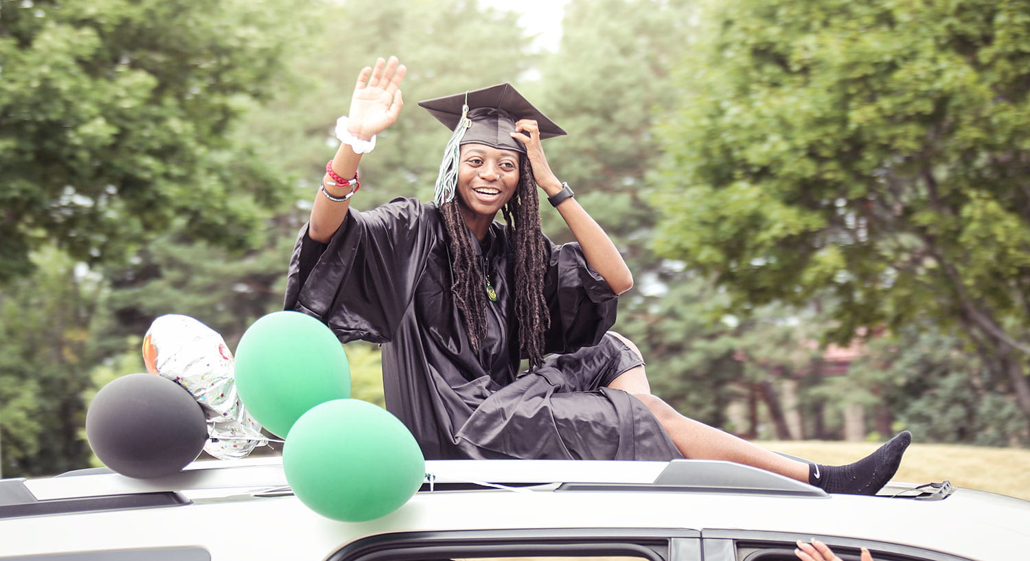 Woman of color in graduation robes on top of her car at UW-Green Bay Graducation Drive-Thru Experience