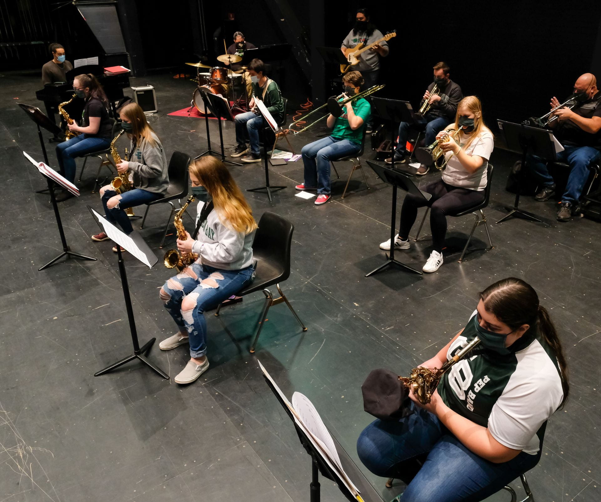 Photo of UW-Green Bay students in Jazz Ensemble class on the main stage at the Weidner Center. Music students use specialized slotted masks, bell covers on brass instruments, and sit 6-feet apart as part of the COVID-19 prevention.