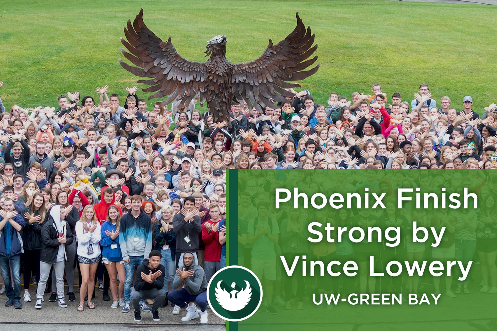 Photo of the UW-Green Bay Phoenix sculpture with students standing in front making a hand phoenix by interlocking their hands together with the words, "Phoenix Finish Strong by Vince Lowery."