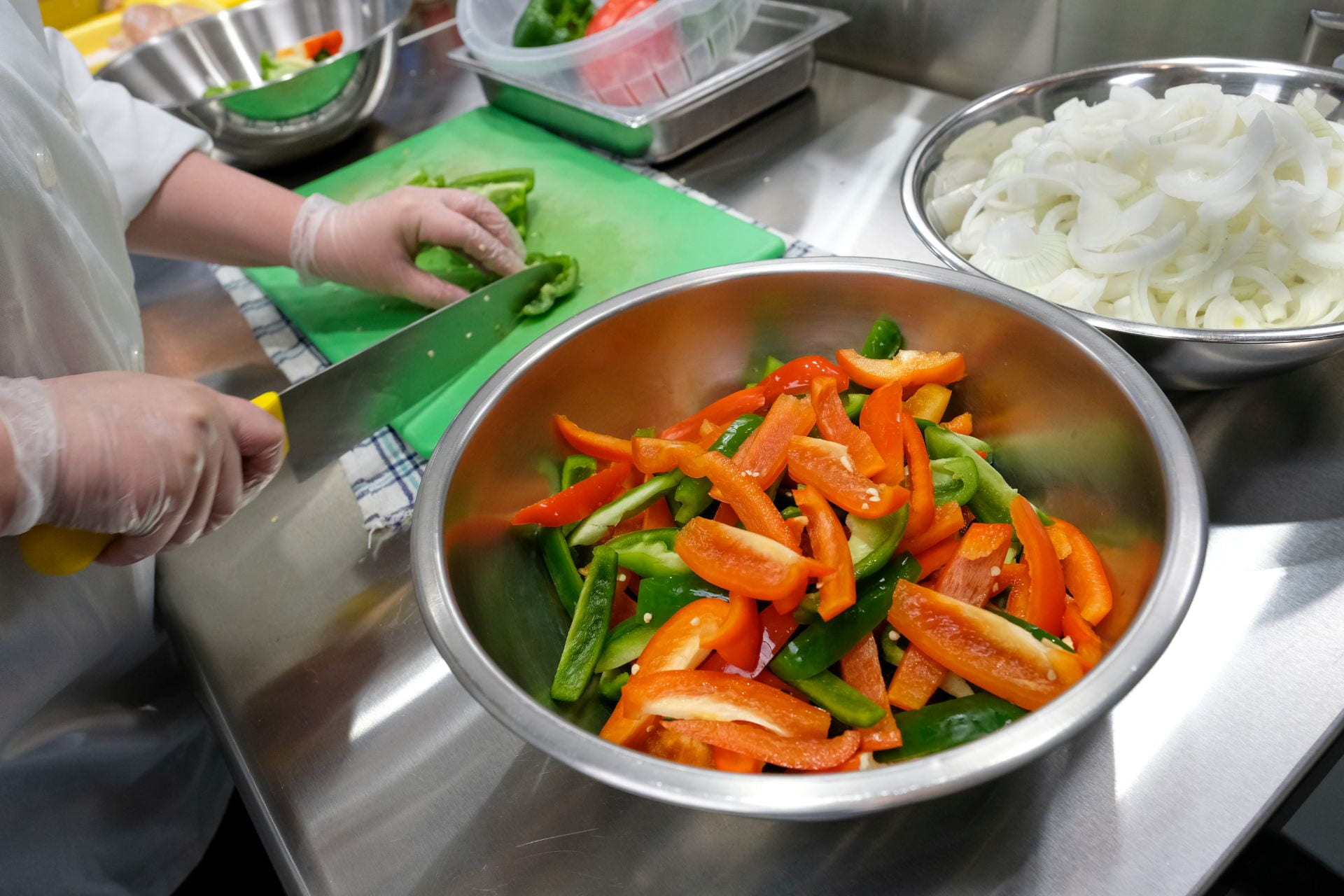 A student in Students in Quantity Food Production and Service class slices Bell peppers for the Jamaican Philly sandwiches in the Food Lab at the STEM Center.