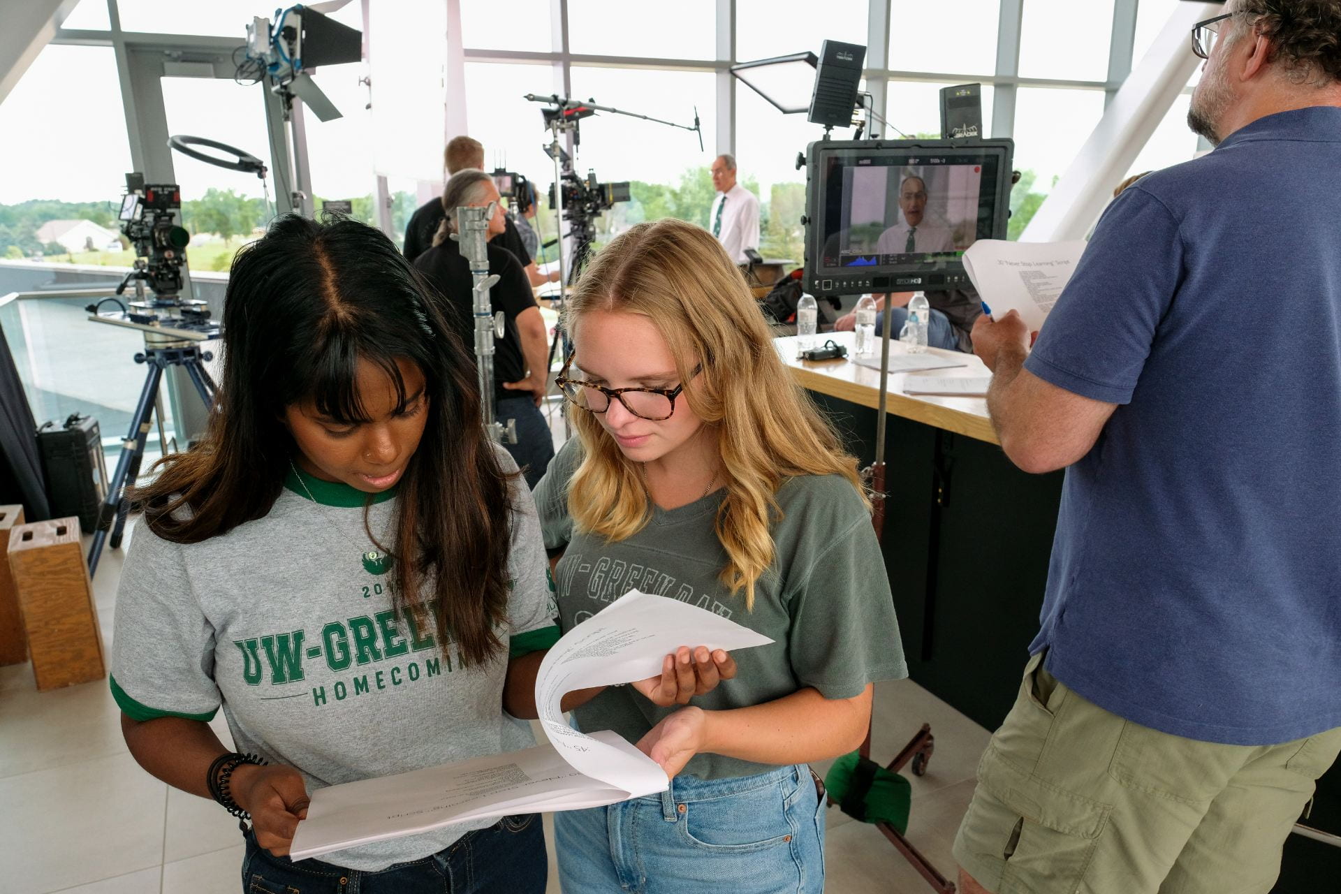 From left, Sound Ritman and Emily Reis, student interns from UW-Green Bay Marketing and University Communication, follow the script as on-screen talent Mike Alexander is filmed during the University of Wisconsin-Green Bay's Never Stop Learning TV commercial at Titletown Tech. 