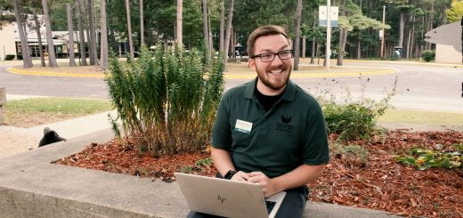 A college counselor sits outside using his laptop and he looks up and smiles during an outdoor meeting at UW-Green Bay, Marinette campus.