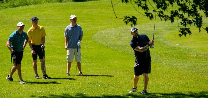 Three golfers watch another golfer hit the ball on the fairway during the UW-Green Bay Scholarship Golf Classic at the Brown County Golf Course.