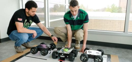 Two Engineering students reset a small four wheeled robot that they have programmed to self park in a parking lot during their demonstration for their final project in Mechatronics Lab at UW-Green Bay.