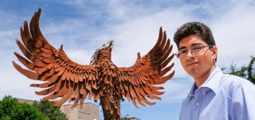 A serious looking computer science student stands next to the phoenix sculpture on a sunny, blue sky day at the UW-Green Bay campus.