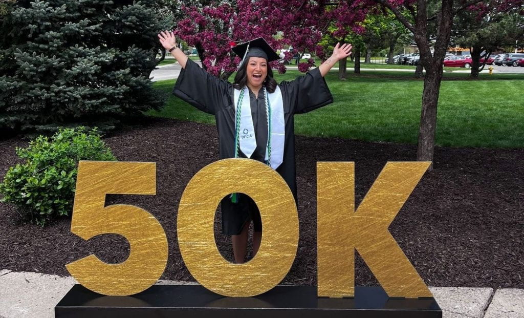 women in graduation regalia poses by large "50K" display