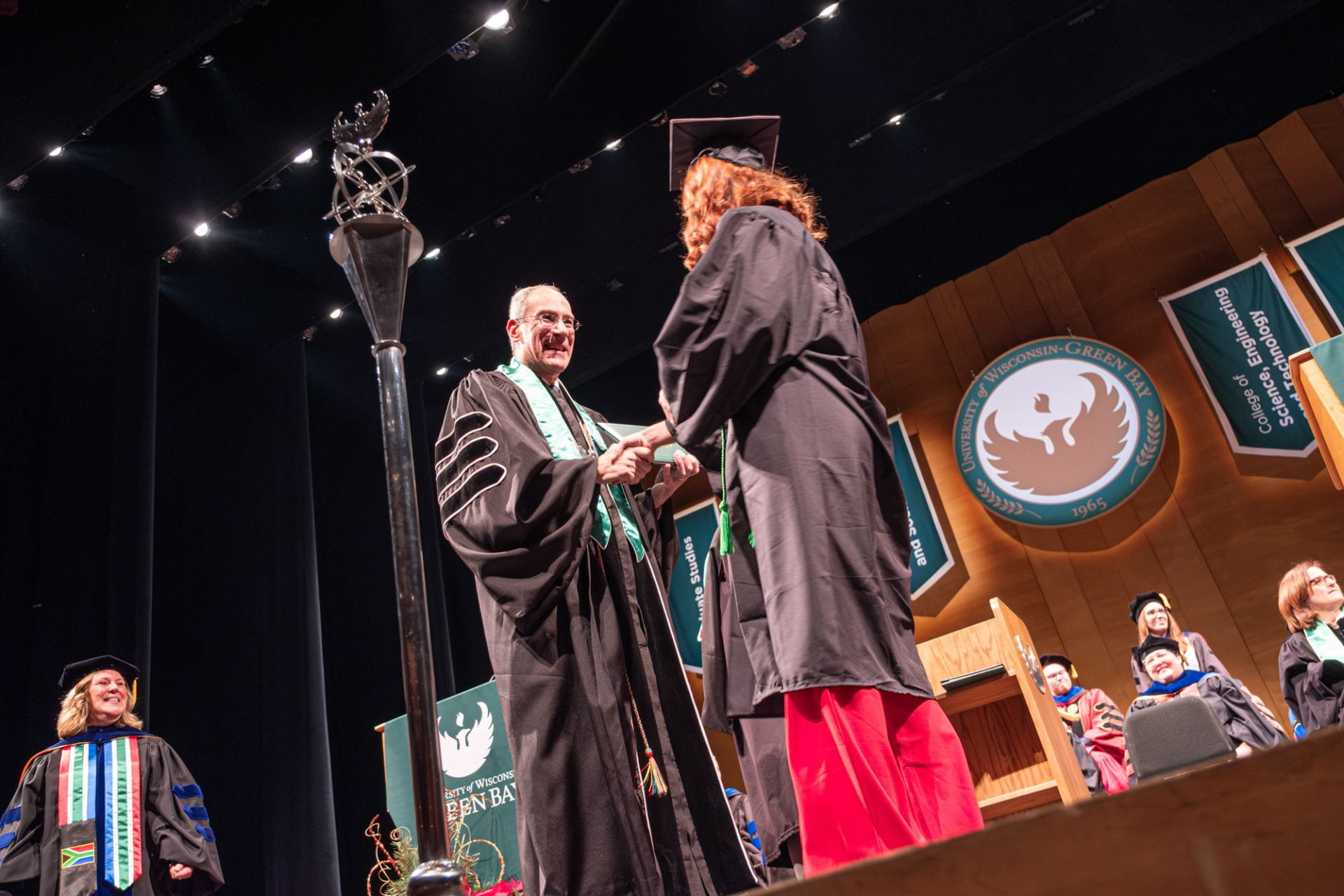 Chancellor Alexander hands a diploma to a new graduate at the Winter 2023 Commencement ceremony.